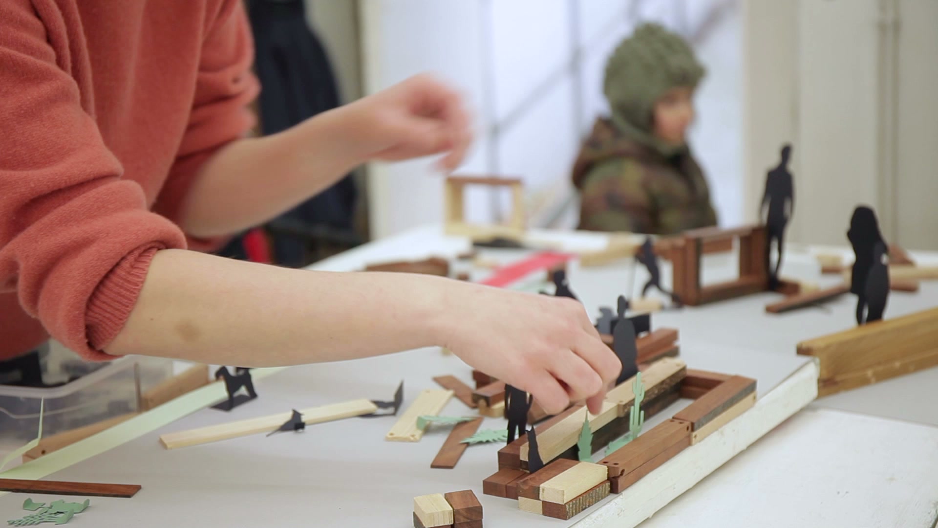 Hands arranging timber pieces in the workshop scale model